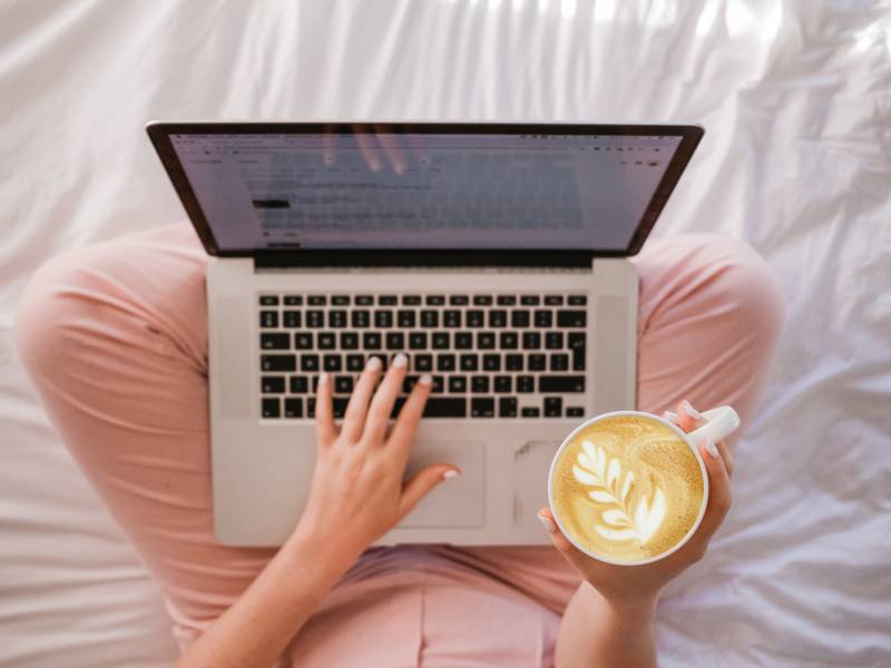 woman sitting on bed with a laptop and coffee